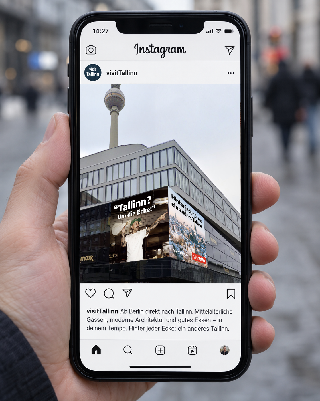 Ühe käega hoitud iPhone’is on Visit Tallinna Instagrami reklaam: Berliini hoone nurgal paiknev reklaam ühendab pitsameistri ja Tallinna vanalinna.